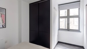 Ein Schlafzimmer mit einem Bett, einem schwarzen Kleiderschrank, einem Fenster mit Jalousien und einem gerahmten Bild an der Wand.