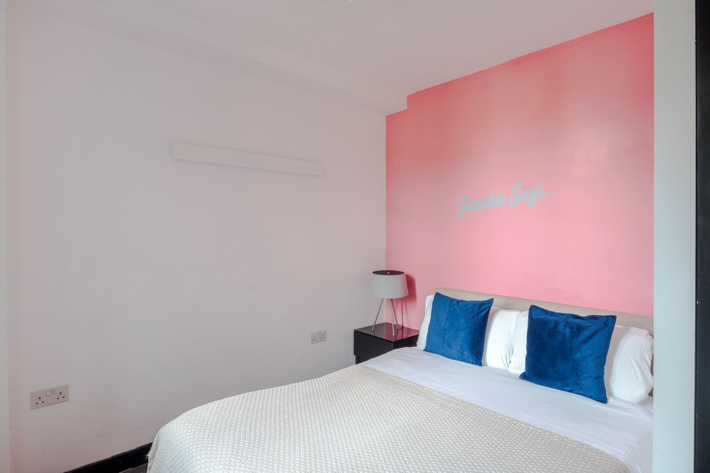 A bedroom with a bed, a nightstand, a lamp, and a wall with a partial text.