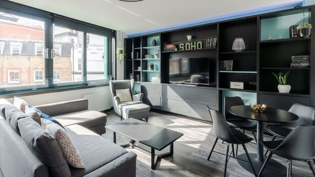 Ein modernes Wohnzimmer mit einer Couch, Sesseln, einem Couchtisch und einem Esstisch mit Stühlen. Ein Bücherregal ist mit Dekorationen dekoriert, und ein Schild trägt die Aufschrift 'SOHO'.