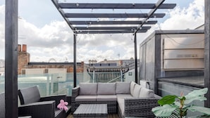 A rooftop terrace with wicker furniture, a glass balustrade, and a view of the cityscape. - The Instagood Penthouse - Covent Garden - by Frankie Says (London)