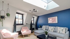 A modern living room with a blue accent wall, a grey sofa, a pink armchair, a black coffee table, and hanging plants. - The Instagood Penthouse - Covent Garden - by Frankie Says (London)