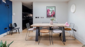 A modern dining area with a skylight, a kitchen in the background, and a poster on the wall. - The Instagood Penthouse - Covent Garden - by Frankie Says (London)