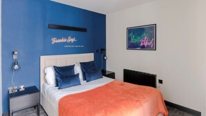A modern bedroom with a blue accent wall, a bed with blue and white bedding, a neon sign, and a framed picture. - The Peaches Cream - Soho - by Frankie Says (London)