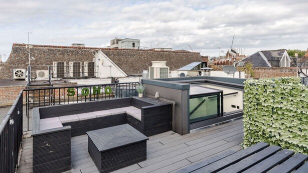 Terraza en la azotea con asientos negros, cerramiento de vidrio y un seto.