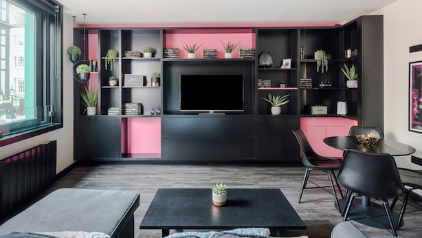 Een moderne woonkamer met een kleurenschema in zwart en roze, met een flatscreen televisie, zwart en roze meubels en verschillende potplanten.