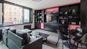 Een moderne woonkamer met een groot raam, zwarte en roze planken, een flatscreen televisie en een eethoek met stoelen.