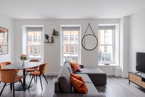 Un salon moderne avec un canapé gris, des fauteuils orange, un miroir rond et un téléviseur.