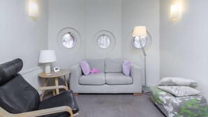 A room with a grey sofa, a black leather chair, a small round table with a lamp, and a floor lamp. - The Aristocrat - Fitzrovia - by Frankie Says (London)