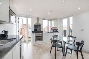 Una cocina moderna con comedor, que incluye una mesa y sillas de vidrio, electrodomésticos de acero inoxidable y ventanas amplias.