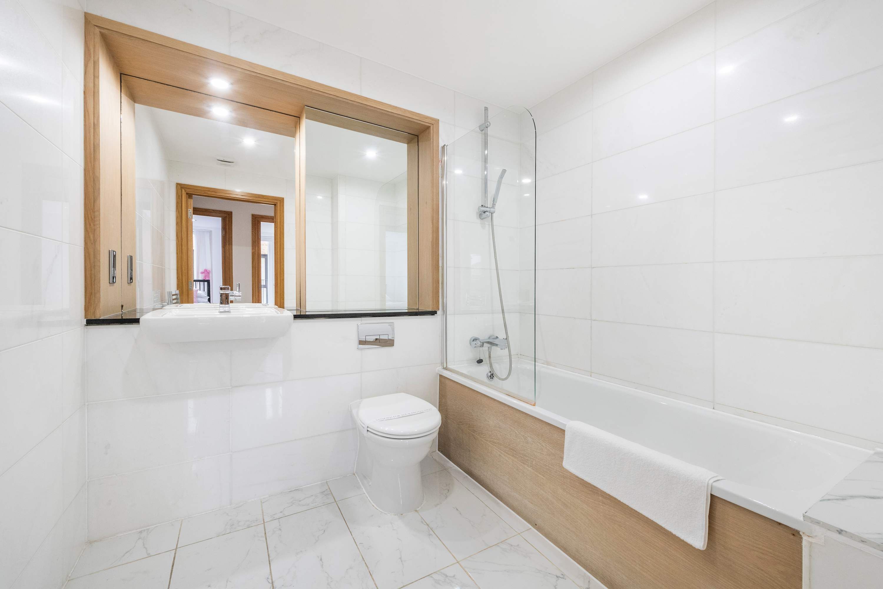 A modern bathroom with a white toilet, a glass-enclosed shower, and a wooden vanity.