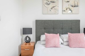 A neatly arranged bedroom with a grey upholstered headboard, a bedside table with a lamp, and a small wooden nightstand. - The Kings Residence - St Pancras - by Frankie Says (London)