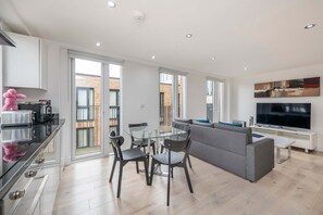 Una sala de estar moderna con una mesa de comedor de vidrio, un sofá gris y un televisor de pantalla plana.