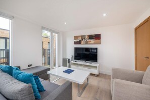 Una sala de estar moderna con un sofá, una mesa de centro, un televisor y un ventanal corredizo que da a un espacio exterior.