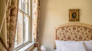 A bedroom with a bed, a nightstand, a lamp, a window with curtains, and a framed picture on the wall. - The Grand Old Boy - Marylebone - by Frankie Says (London)