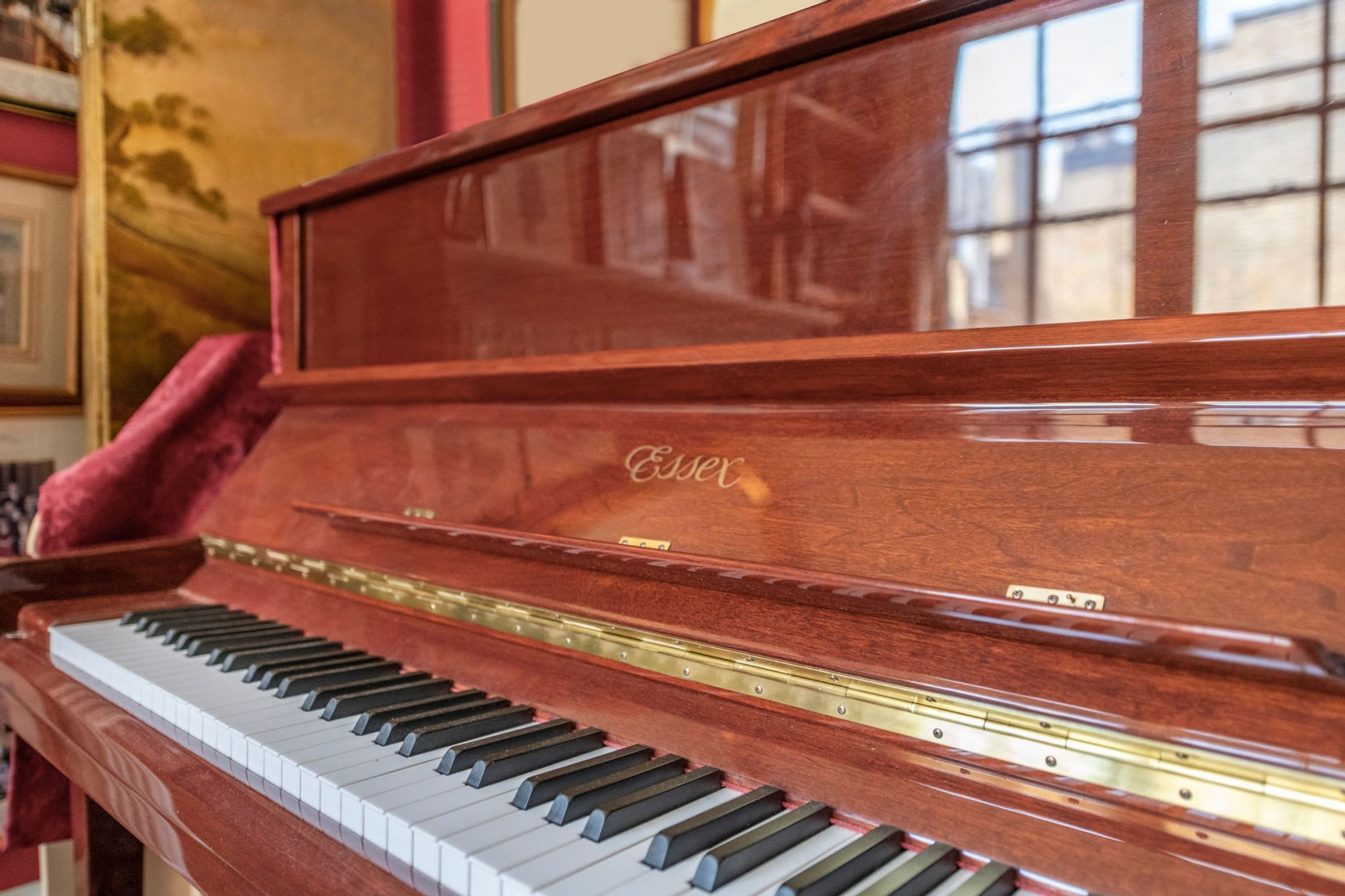 Un piano de cola con un acabado de madera brillante y el nombre de la marca 'Essex' visible en el lateral.