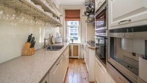 A narrow kitchen with white cabinets, a granite countertop, and stainless steel appliances including a range hood, oven, and microwave. - The Grand Old Boy - Marylebone - by Frankie Says (London)