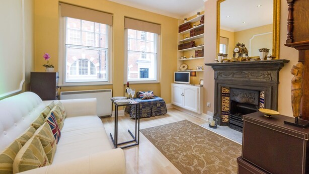 A well-lit room with a sofa, a small table, a fireplace, and a bookshelf. - The Vintage - Fitzrovia - by Frankie Says (London)