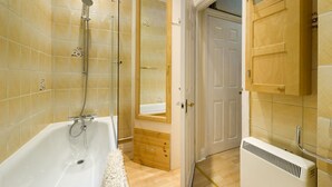 A modern bathroom with a bathtub, shower, and a wooden cabinet with a medical cross symbol. - The Vintage - Fitzrovia - by Frankie Says (London)