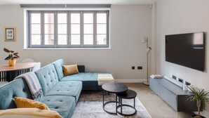 Un salon moderne avec un canapé d’angle, un téléviseur à écran plat, une table à manger et une grande fenêtre.