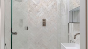 Une salle de bain moderne avec une douche à parois de verre, un lavabo blanc et un mur recouvert de carreaux disposés en motif chevrons.