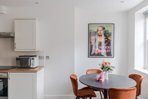 Una cocina moderna con armarios blancos, un microondas y un comedor con una mesa redonda y sillas naranjas.