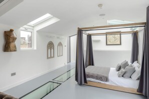 Un dormitorio moderno con piso de vidrio hacia el nivel inferior, una cama con dosel y vistas a la ciudad.