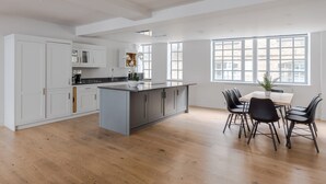 A spacious kitchen with a large island, white cabinetry, and a dining area with black chairs. - Circus of Colour - Farringdon - by Frankie Says (London)