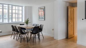 A modern dining area with a wooden table and black chairs, large windows, and a door. - Circus of Colour - Farringdon - by Frankie Says (London)