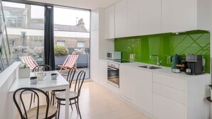 A modern kitchen with white cabinets, a green backsplash, and a dining area with striped chairs. - A Starry Starry Night - Borough - by Frankie Says (London)