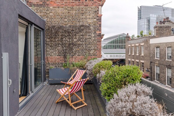 A rooftop terrace with two striped lounge chairs, a brick wall, and a view of a building with a sign that reads "BORDO."