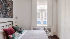 A bedroom with a bed, a window with a view of buildings, a wall-mounted artwork, and a white door. - A Starry Starry Night - Borough - by Frankie Says (London)