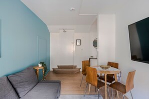 Uma sala de estar moderna com um sofá cinza, mesa de jantar de madeira com quatro cadeiras e uma escada que leva a outro cômodo.