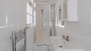 A narrow bathroom with a shower, a sink, and a mirror. - Wonderland - Fitzrovia - by Frankie Says (London)