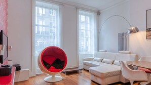A modern living room with a red chair, white sofa, and a dining table. - The Red Room Apartment - Fitzrovia - by Frankie Says (London)
