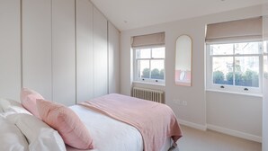 A bedroom with a bed, a radiator, and two windows with blinds. - Parkside House - Regent s Park - by Frankie Says (London)