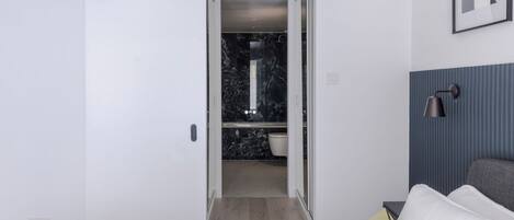 A bedroom with a bed, a bedside table, a lamp, and a sliding door leading to a bathroom with a marble floor and a toilet.