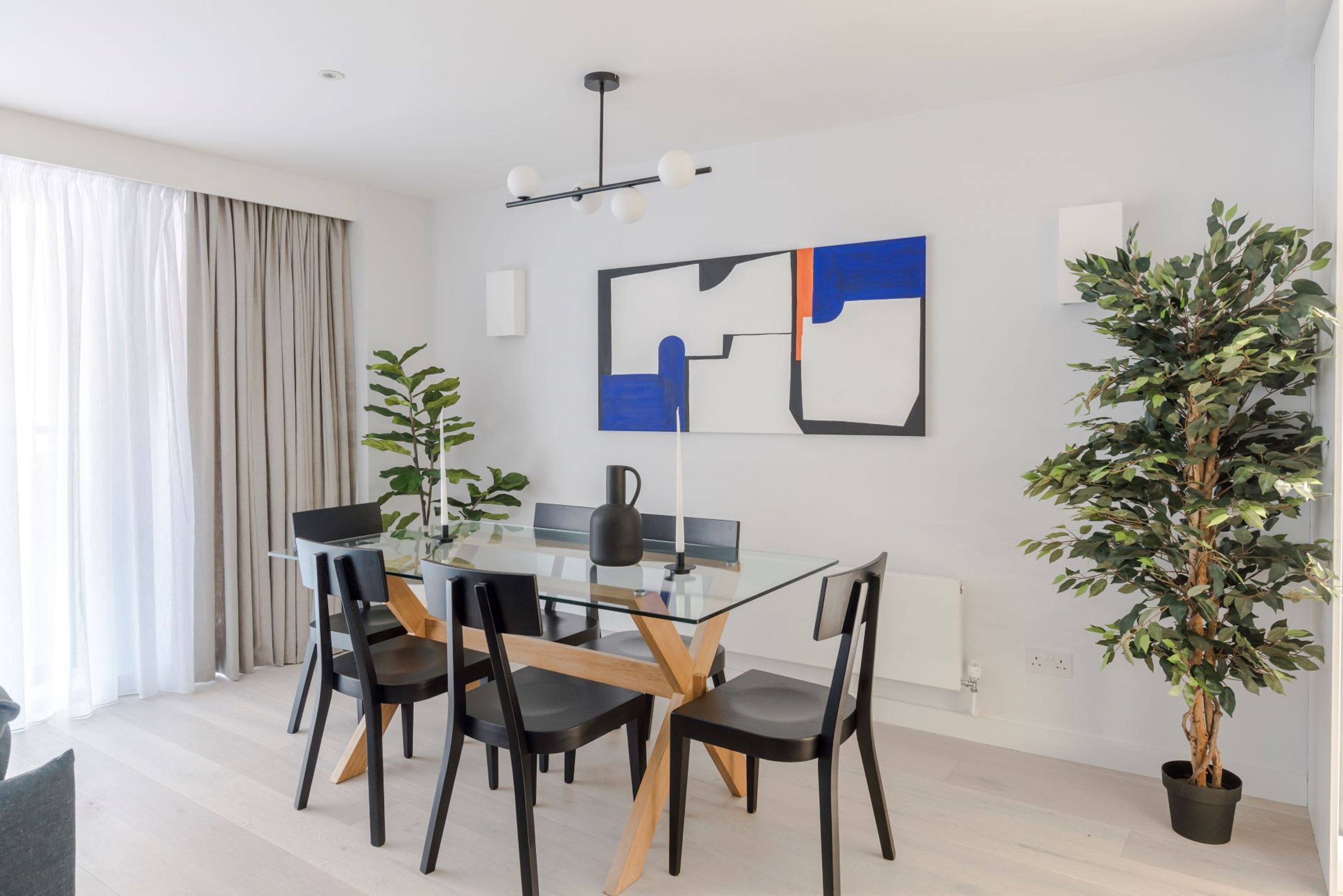 Un espace repas moderne avec une table en verre, des chaises noires et en bois, un luminaire suspendu noir et une plante en pot.