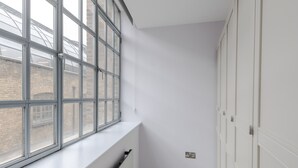 Une pièce d’angle avec une grande fenêtre, des murs blancs et un radiateur.