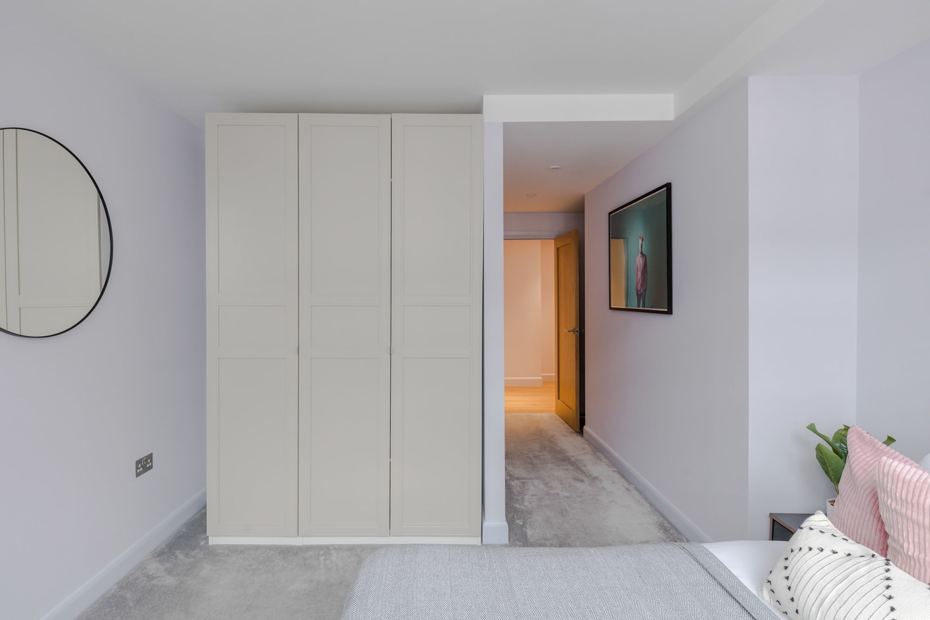 A bedroom with a bed, a wardrobe, a mirror, and a painting on the wall.