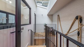A modern interior with a wooden staircase, black metal railings, and a skylight. - The Insta Playhouse - Covent Garden - by Frankie Says (London)