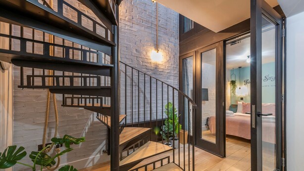 A modern interior with a spiral staircase, a brick wall, and a cozy bedroom with a bed and a plant. - The Insta Playhouse - Covent Garden - by Frankie Says (London)