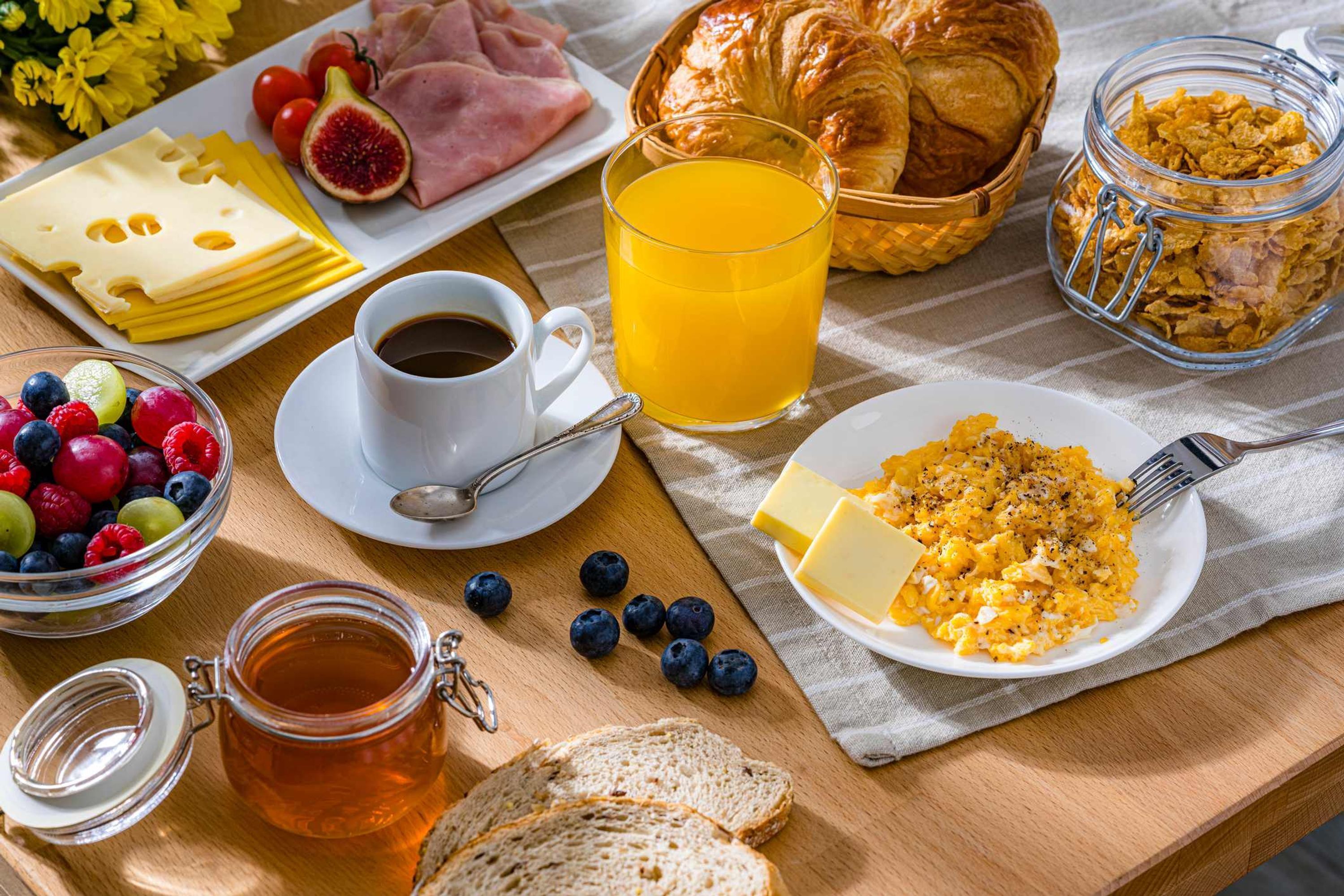 Ein Frühstücksbuffet mit Käse, Schinken, Croissants, Obst und einem Glas Orangensaft.