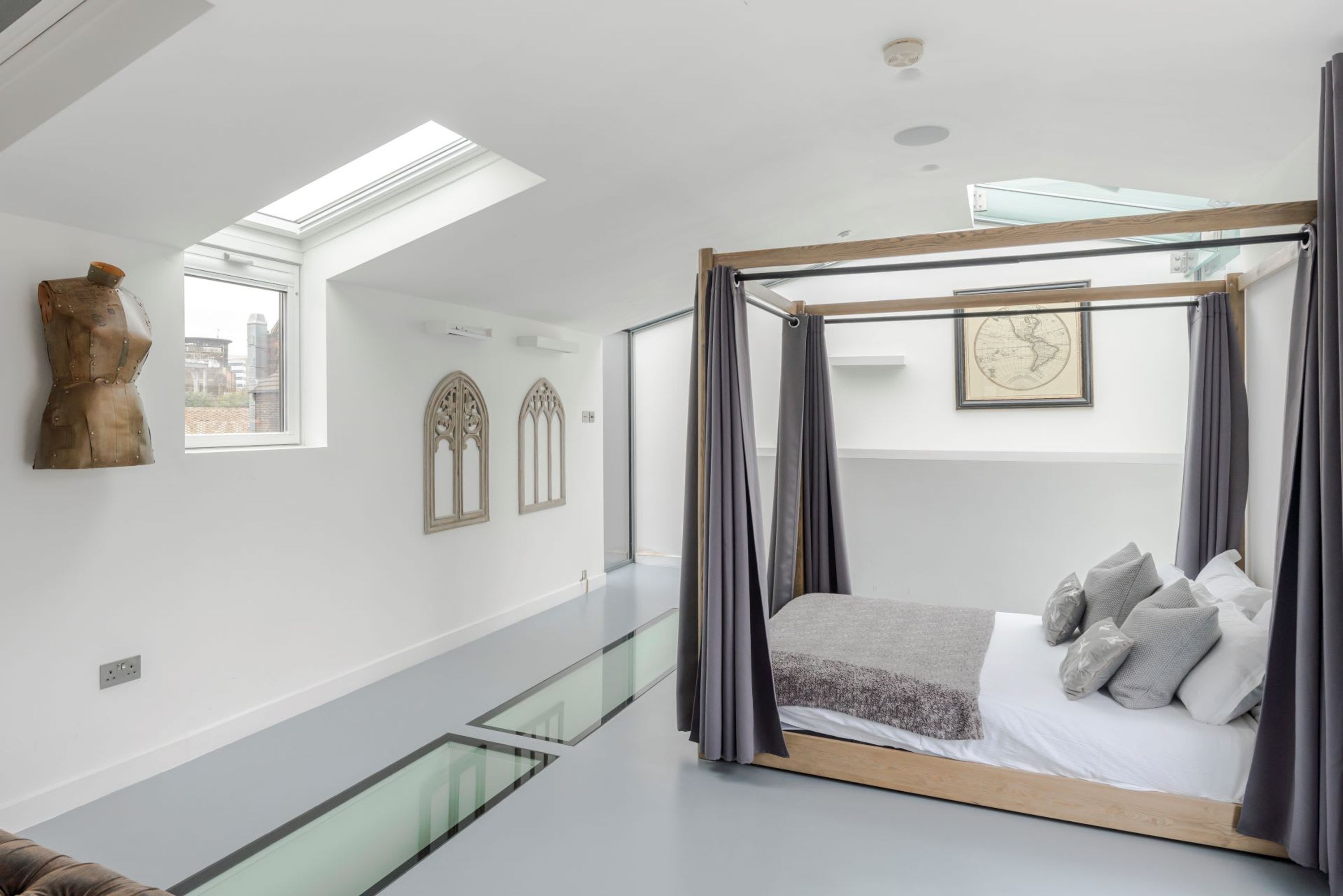 Quarto moderno com piso de vidro para o nível inferior, cama de dossel e vista para a cidade.