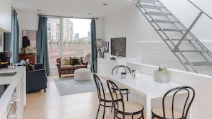 Un apartamento moderno con comedor, sala de estar con sofá y reposapiés, cocina y tragaluz.