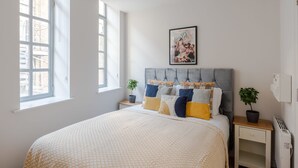 A bedroom with a large bed, a headboard, a nightstand, a potted plant, and a window. - Sweet Dreams - Farringdon - by Frankie Says (London)