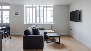 A modern living room with a sofa, a coffee table, and a TV mounted on the wall. - London s Calling - Farringdon - by Frankie Says (London)