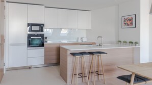 A modern kitchen with white cabinets, a built-in microwave, and a wooden island with bar stools. - Zen Sanctuary - Soho - by Frankie Says (London)