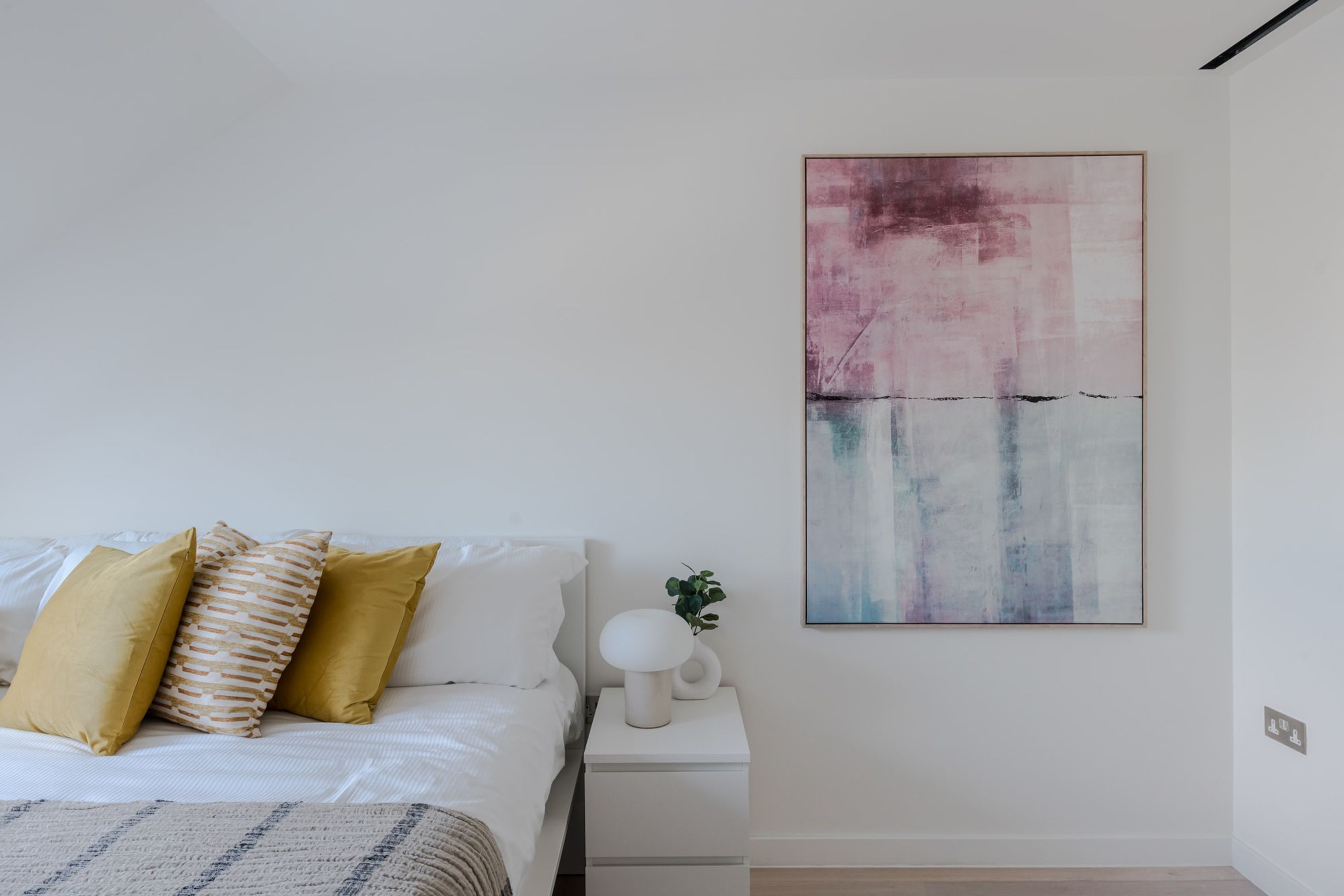 A modern bedroom with a bed, white nightstand, and a large abstract painting.