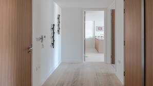 A hallway with wooden doors, a light-colored floor, and a view into a room with a kitchen area. - Zen Sanctuary - Soho - by Frankie Says (London)