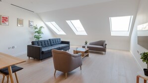 A modern living room with a sofa, armchair, and coffee table, featuring skylights and a potted plant. - Zen Sanctuary - Soho - by Frankie Says (London)